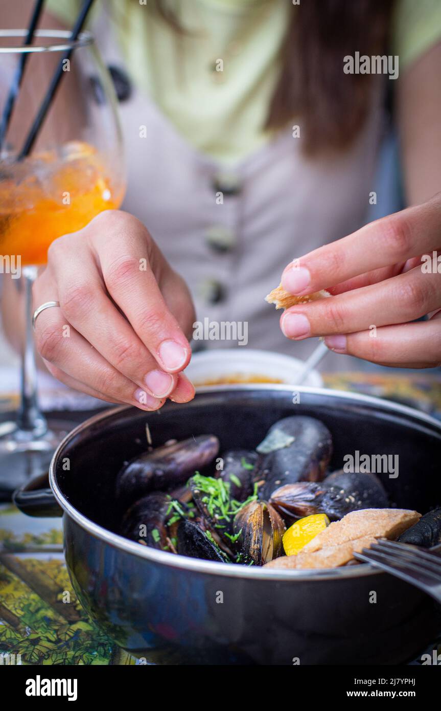 Eine junge Frau isst Meeresfrüchte und trinkt einen Cocktail. Das Konzept eines Urlaubs auf See. Vertikales Foto. Stockfoto