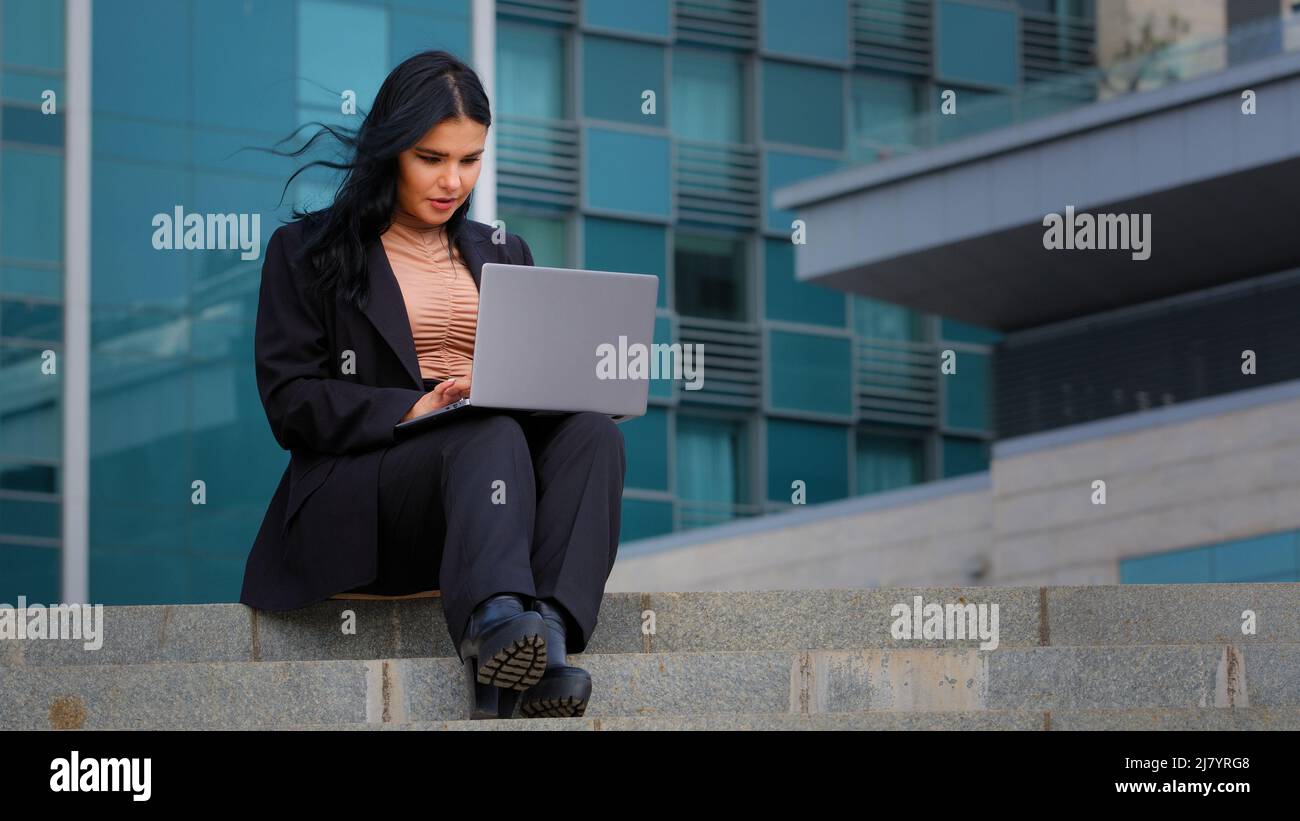 Junge Geschäftsfrau Freiberuflerin sitzt im Freien arbeiten an Internet-Typisierung auf Laptop mit Computer-Technologie tun Online-Arbeit Senden von SMS Stockfoto