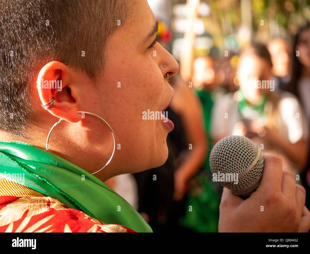 Medellin, Antioquia, Kolumbien - März 8 2022: Rasierte Frau mit großen Ohrringen singt auf der Straße mit einem Mikrofon Stockfoto