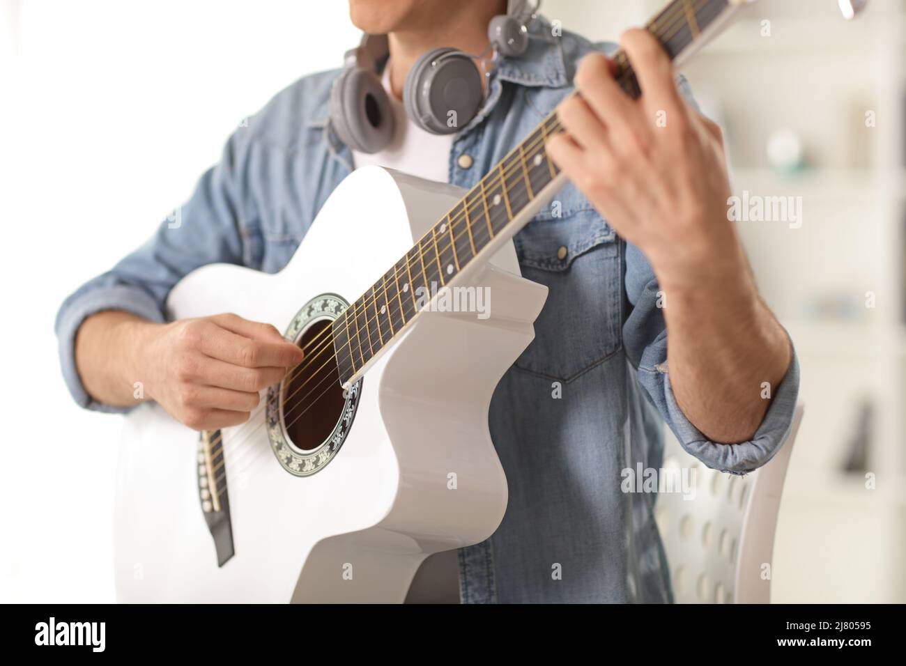 Eine Aufnahme eines jungen Mannes, der eine weiße Akustikgitarre spielt und auf einem Stuhl sitzt Stockfoto