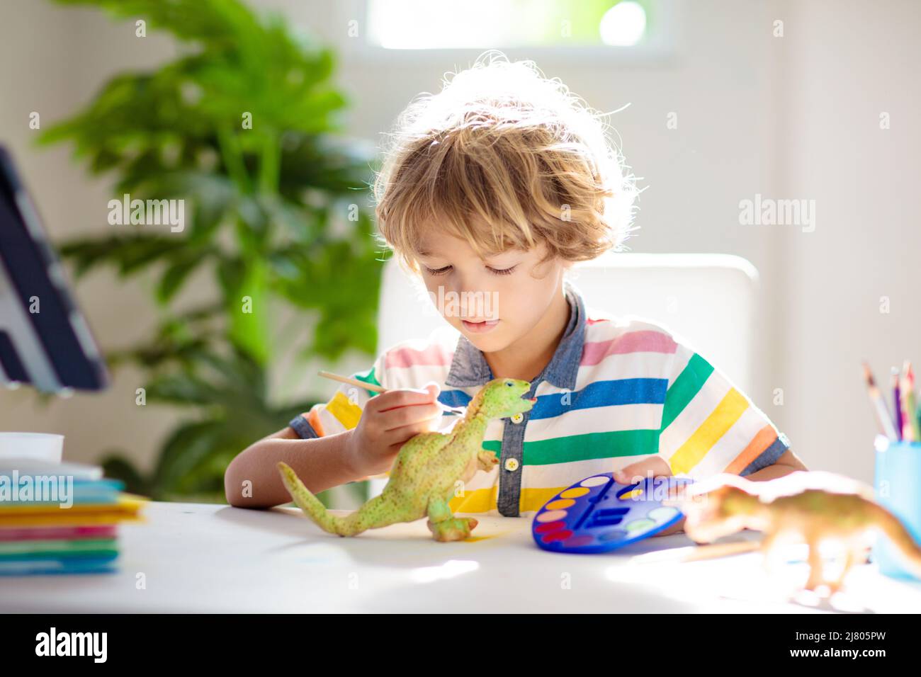 Online-Fernunterricht. Schulkinder mit Computer, die mit dem Lehrer und der Klassengruppe über Videokonferenzen chatten. Kind Färbung Ton Dinosaurier. Stockfoto