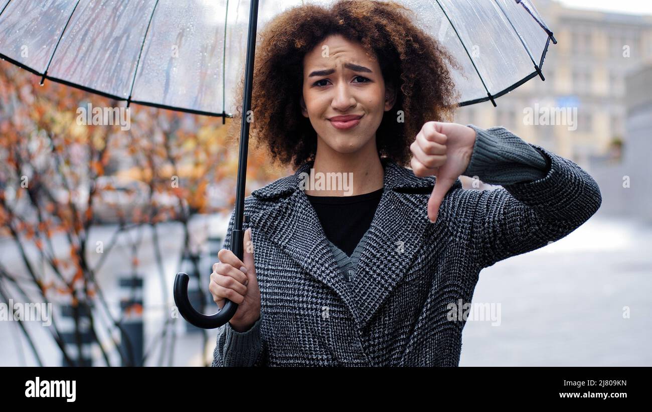 afroamerikanische traurige Mädchen Frau mit lockigen Haaren mit transparentem Regenschirm zeigt Geste der Ablehnung Ablehnung Ablehnung Ablehnung Uneinigkeit Daumen nach unten negativ Stockfoto