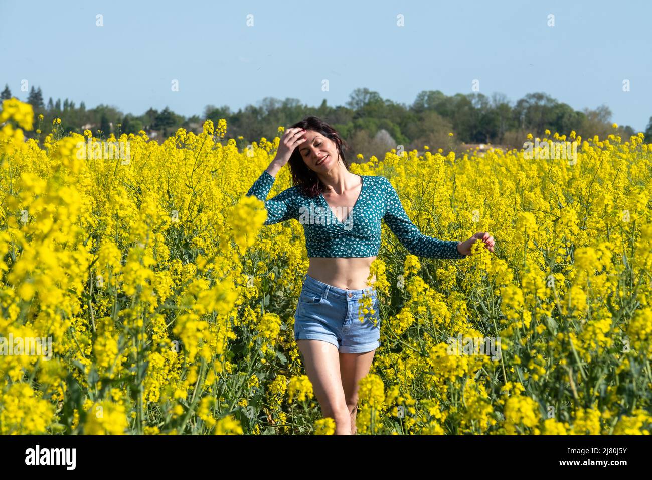 Lächelnde Frau, die im Frühjahr durch ein Rapsfeld geht, Frankreich Stockfoto