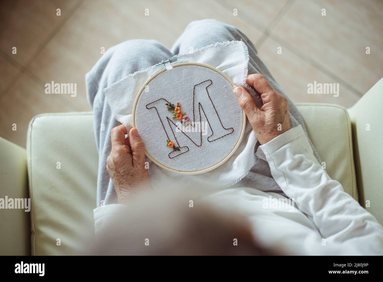 Ansicht von oben einer Frau, die einen Stickrahmen mit dem Buchstaben M hält Stockfoto