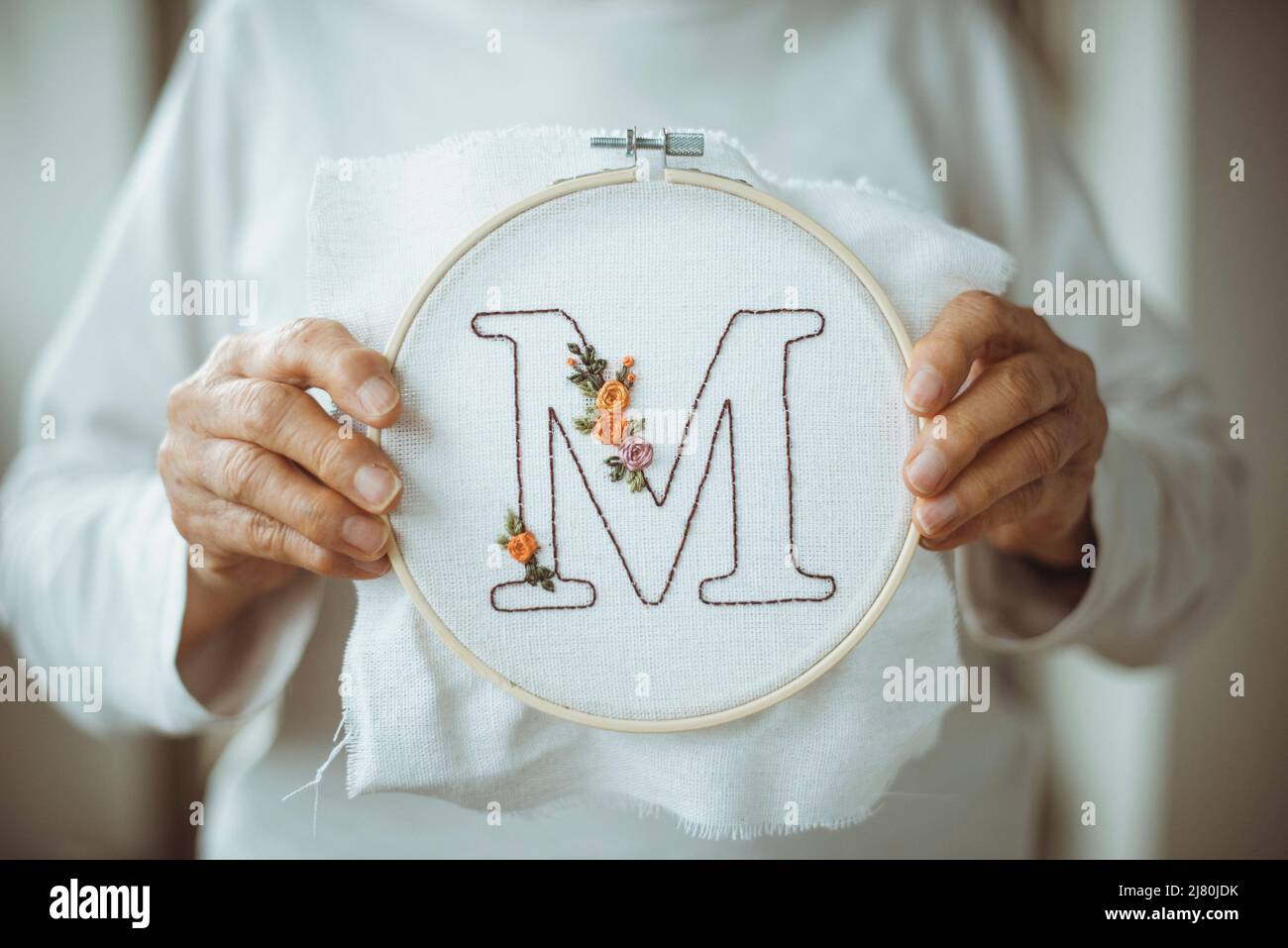 Ältere Frau mit einem Stickrahmen mit dem Buchstaben M Stockfoto