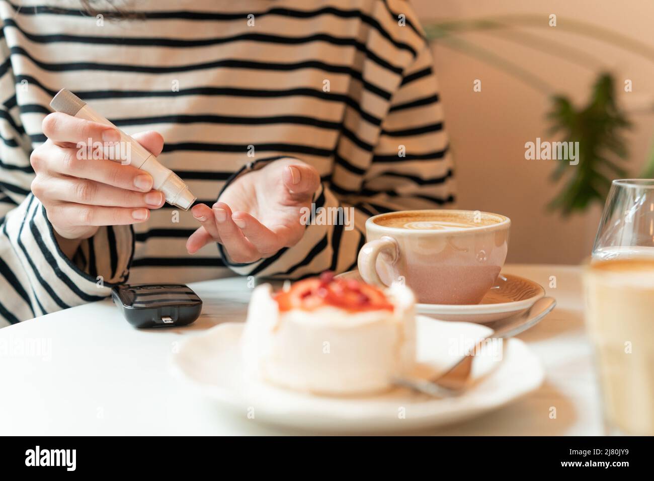 Diabetische Frau, die vor dem Essen an einem Tisch sitzt und den Blutzuckerspiegel in einem Café testet Stockfoto