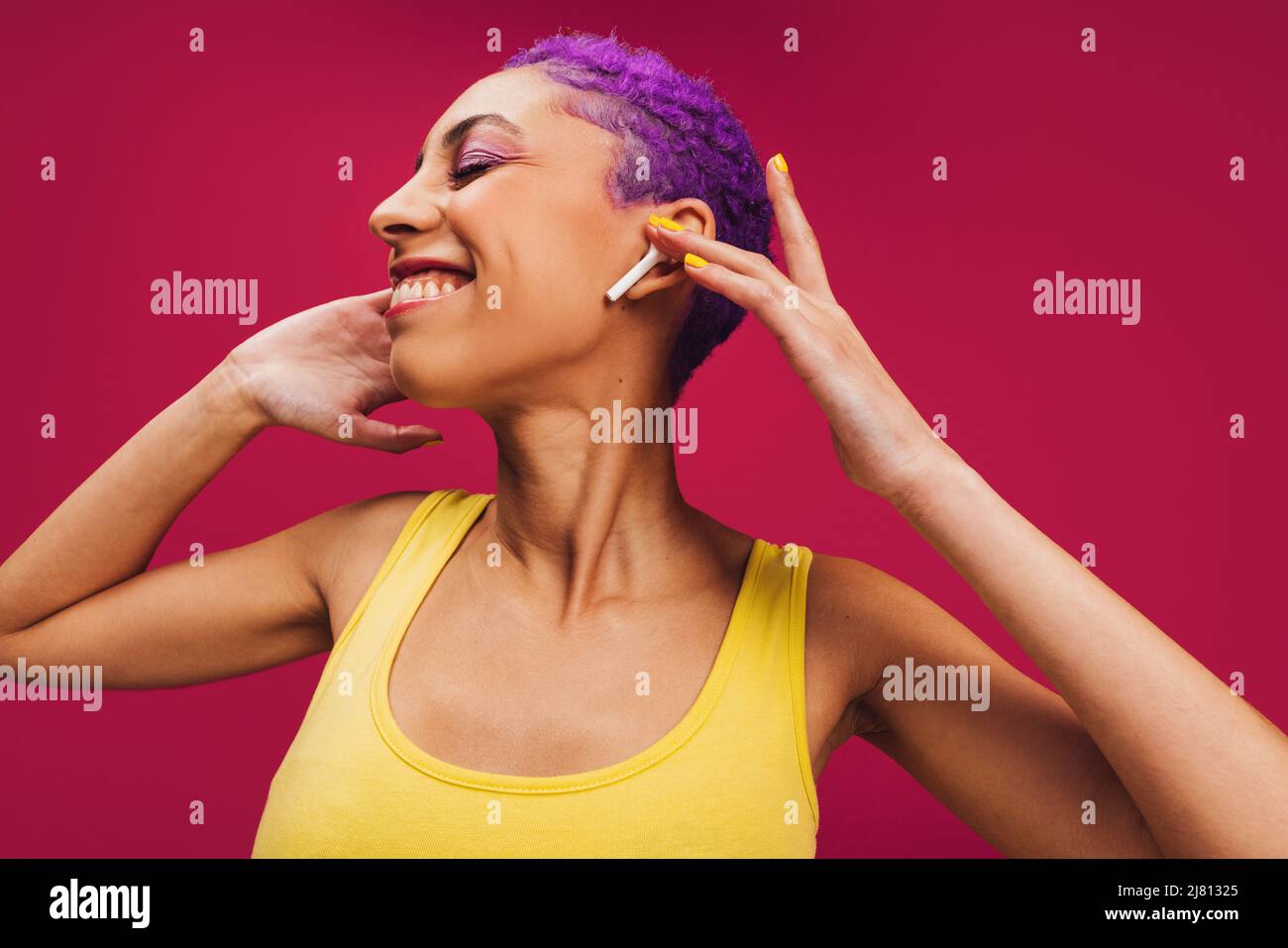 Nur fröhliche Musik. Eine unbeschwerte junge Frau berührt ihre kabellosen Ohrhörer, während sie ihr Lieblingslied hört. Frau mit lila Haaren lächelt fröhlich Stockfoto