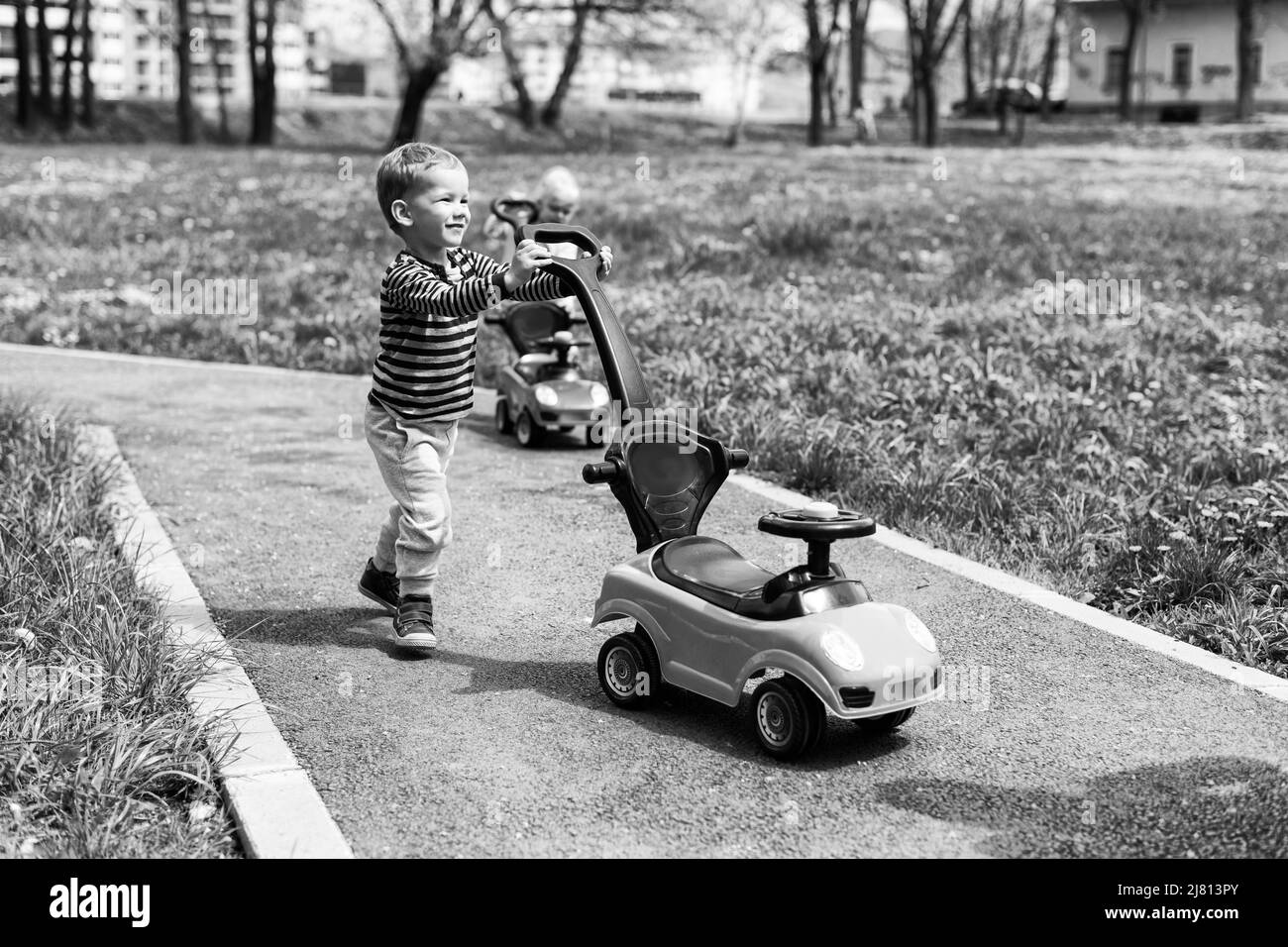 Boy spielt mit einem Spielzeugauto im Freien im Park - Ein Happy Boy fährt ein Spielzeugauto auf der Straße Stockfoto