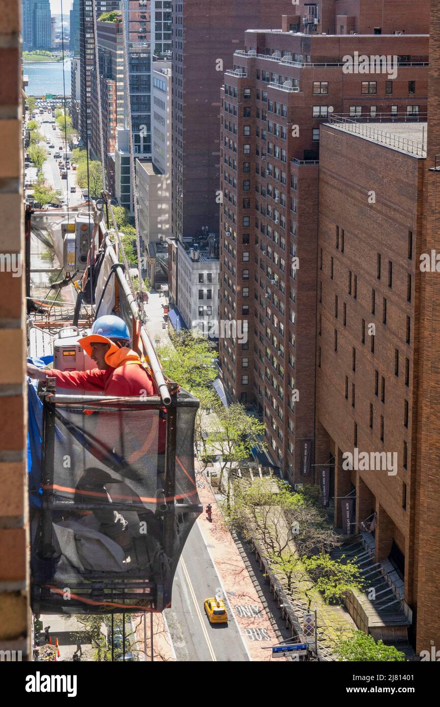 Bauarbeiter hoch über einer städtischen Straße in New York City in einem Hängekorb, Midtown Manhattan, USA 2022 Stockfoto