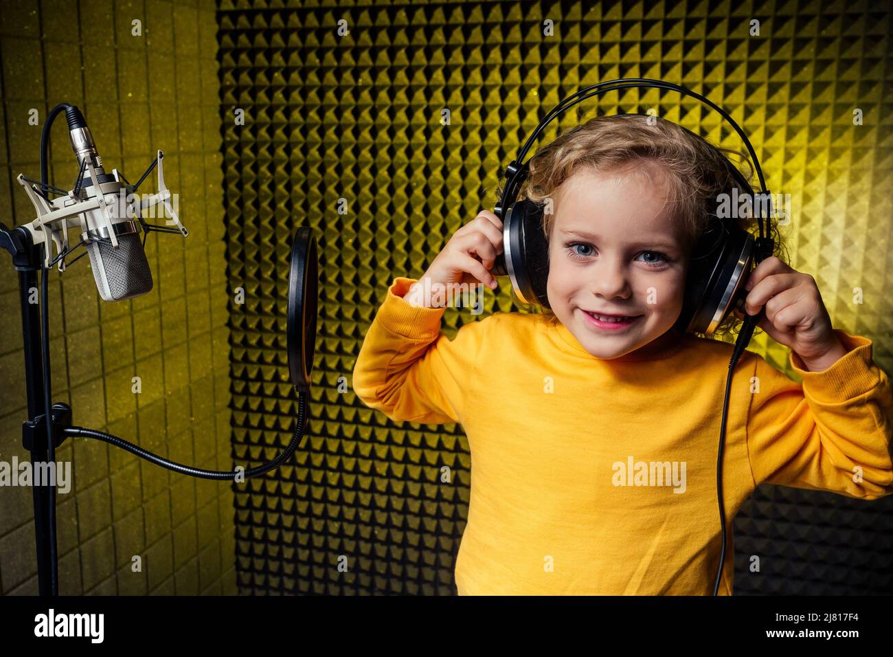 Mädchen blonde lockige Frisur Star-Sängerin Künstler in einer gelben Bluse mit Kopfhörer Aufnahme neuer Song mit Mikrofon. Stockfoto
