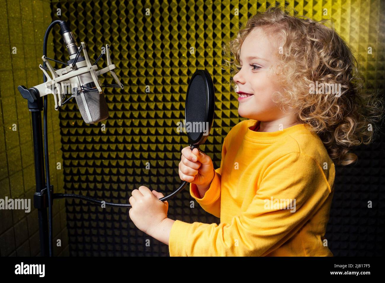 Mädchen blonde lockige Frisur Star-Sängerin Künstler in einer gelben Bluse mit Kopfhörer Aufnahme neuer Song mit Mikrofon. Stockfoto