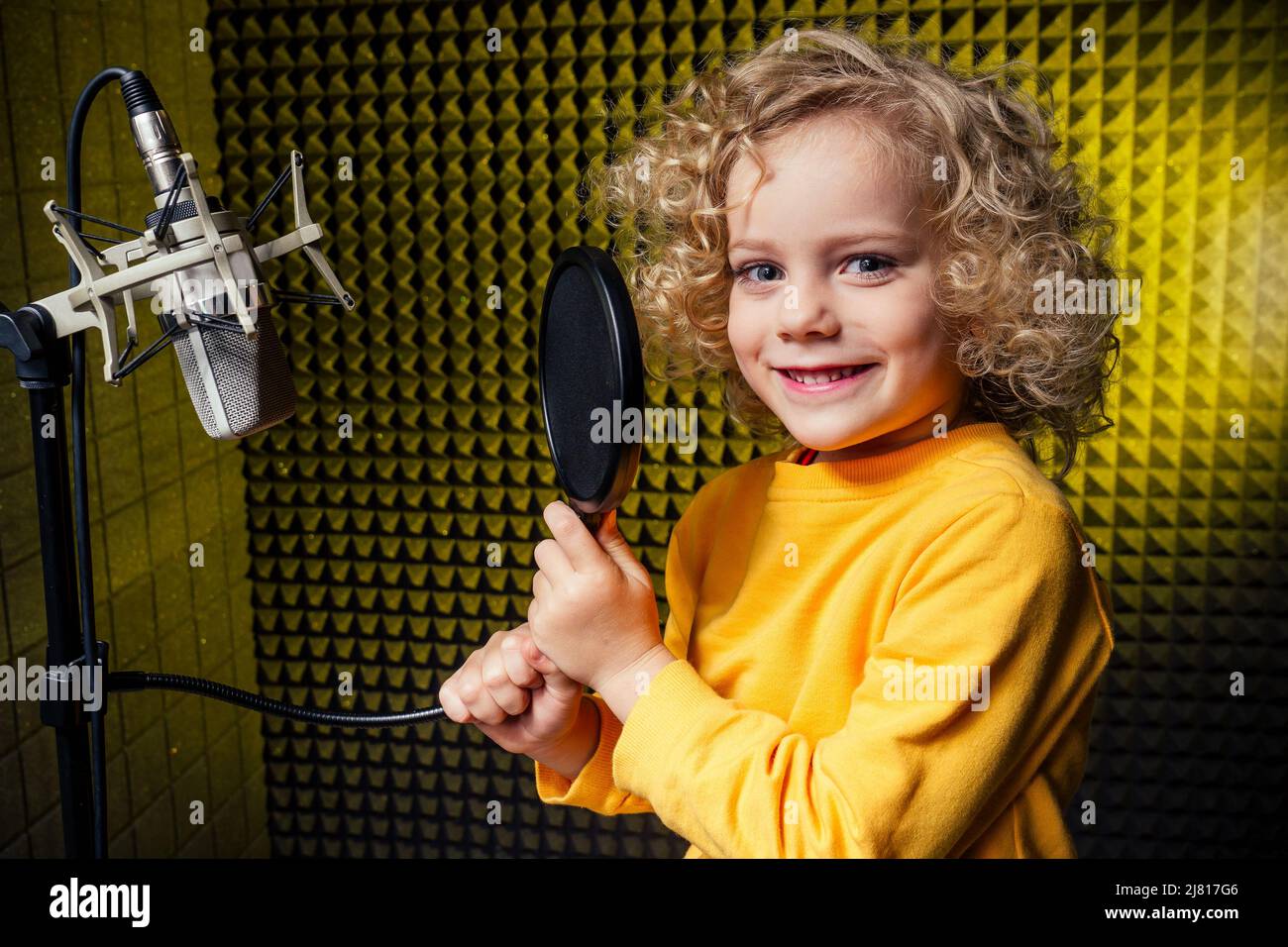 Mädchen blonde lockige Frisur Star-Sängerin Künstler in einer gelben Bluse mit Kopfhörer Aufnahme neuer Song mit Mikrofon. Stockfoto