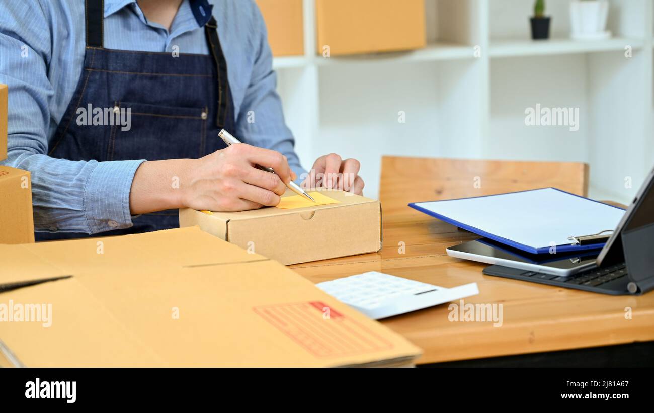 Männlicher Ladenbesitzer, der das Bestellpaket des Kunden für die Lieferung in seinem Lagerraum verpackt. Zugeschnittenes Bild Stockfoto