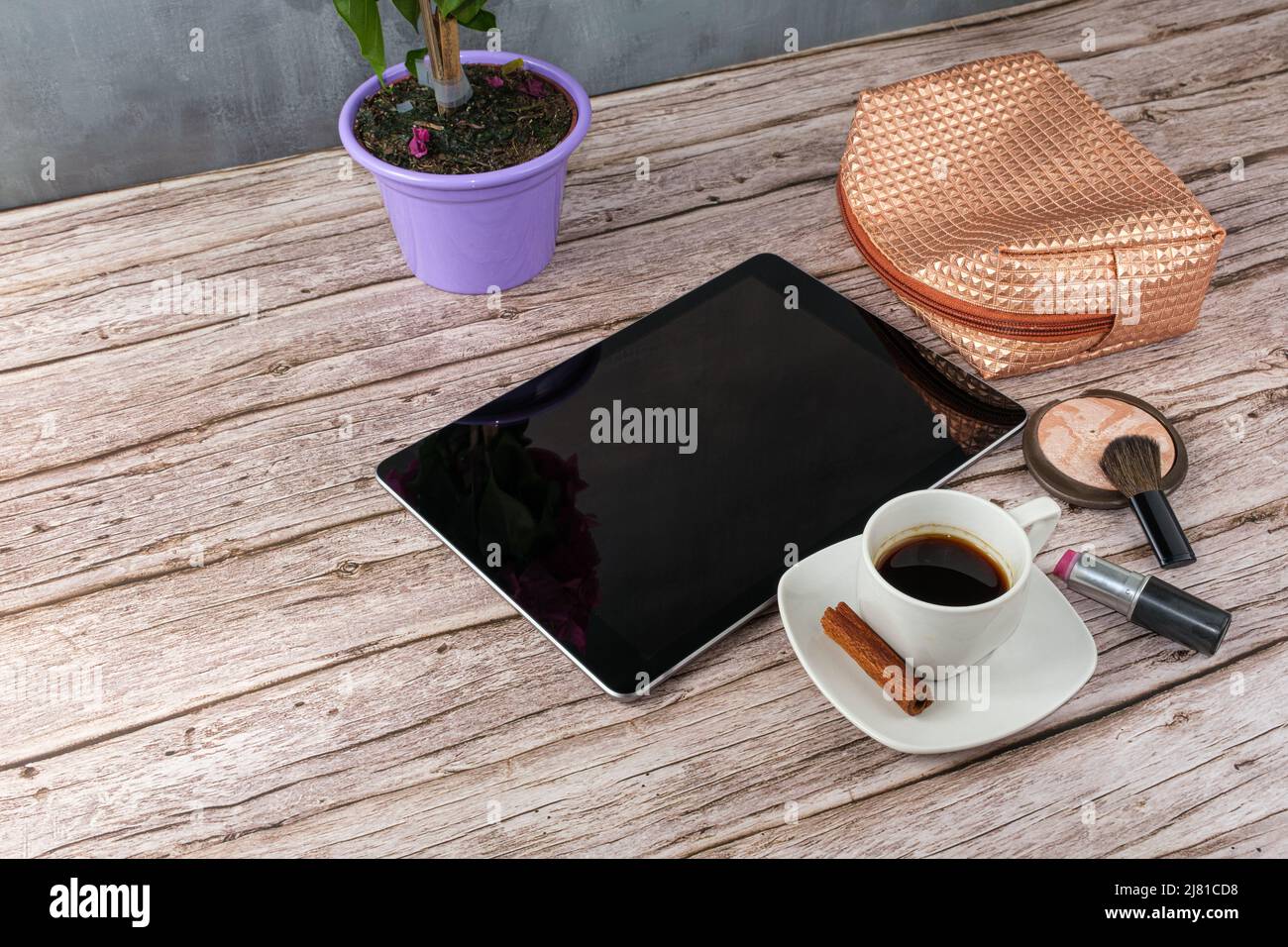 Tablet auf dem Tisch, umgeben von Kaffeetasse, Lippenstift und Make-up-Beutel. Stockfoto