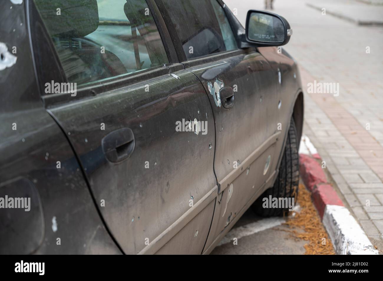 Eine Limousine mit Durchgangslöchern aus Schrapnel steht auf einem Parkplatz. Das geschälte Auto. Der Krieg in der Ukraine. Folgen des Beschuss von Zivilisten Clust Stockfoto