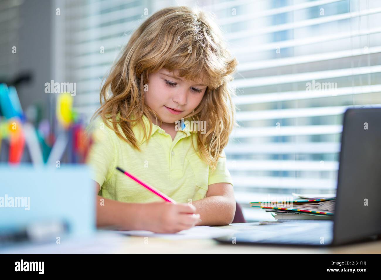Kind schreibt in der Schule. Nette Schüler schreiben am Schreibtisch im Klassenzimmer der Schule. Netter Junge, der Hausaufgaben macht, schreibt und malt. Vorschulkinder mit Stockfoto