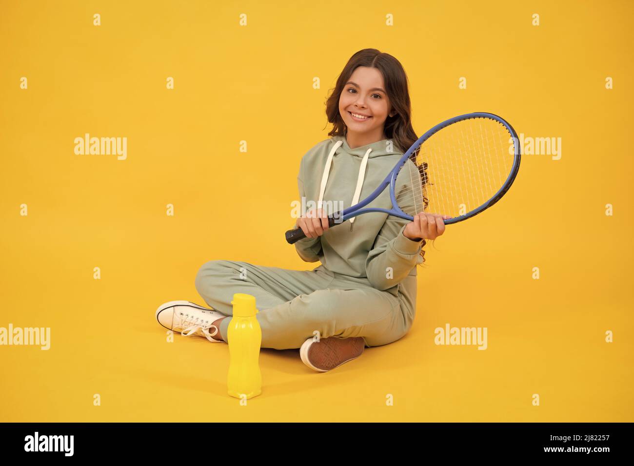 Kind sitzen mit Schläger und Wasserflasche. Kind mit Tennisschläger. Teenager-Mädchen nach dem Sporttraining. Stockfoto