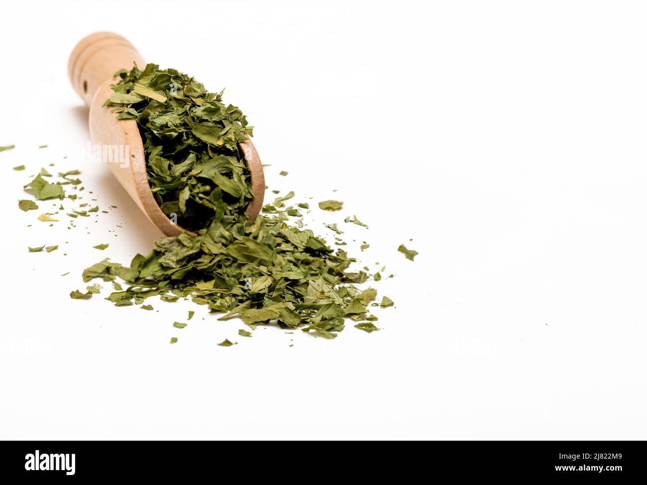 Bambusholz Messlöffel gefüllt mit getrockneter Petersilie isoliert auf weißem Hintergrund ausgewählter Fokus Stockfoto