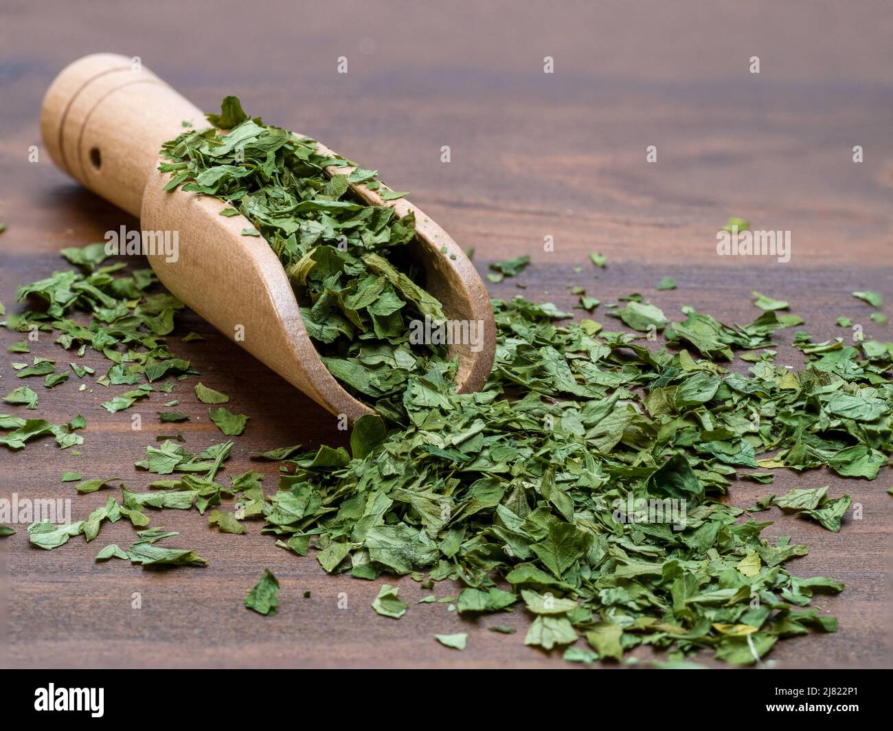 Antikes Holz Messlöffel gefüllt mit getrockneter Petersilie isoliert auf einem natürlichen Holztisch Stockfoto