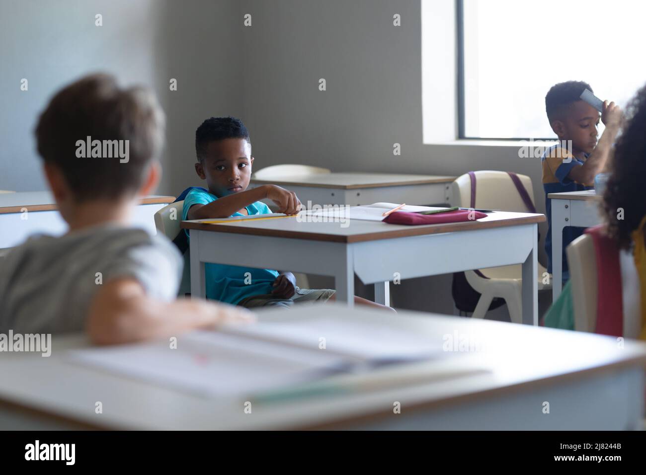 Multirassische Grundschüler sitzen im Klassenzimmer am Schreibtisch Stockfoto