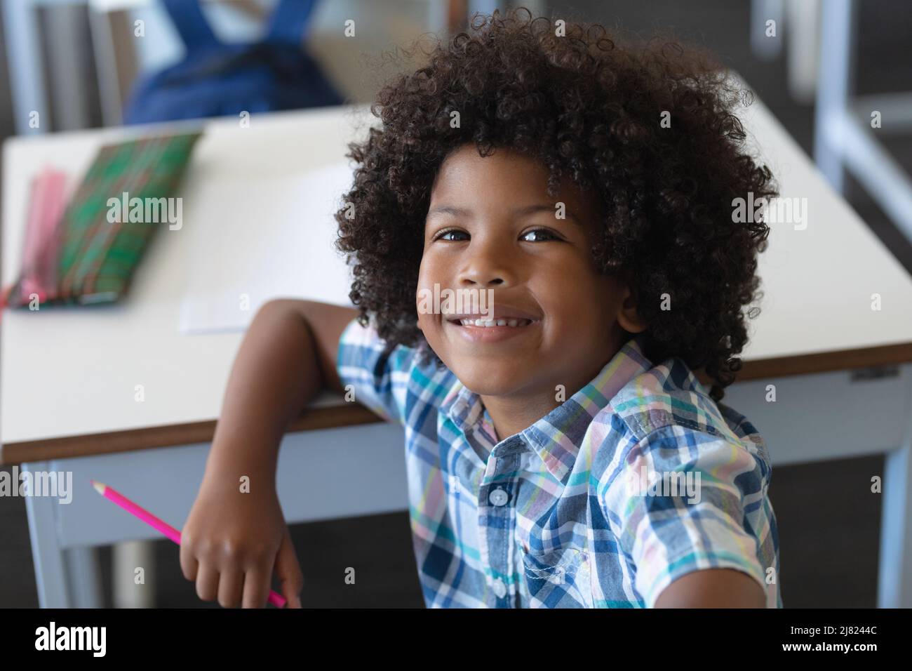 Porträt eines lächelnden afroamerikanischen Grundschuljungen mit Afro-Frisur am Schreibtisch Stockfoto