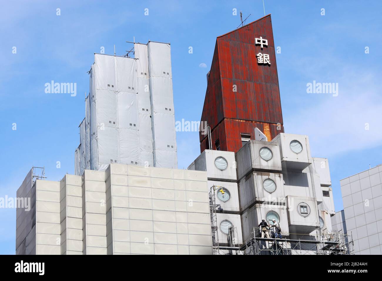 TOKIO, JAPAN - 10. Mai 2022: Ansicht der Arbeiter in der Nähe des Nakagin Capsule Tower, der unter dem Abriss steht und von einem Zaun bedeckt ist, schalldichte Platten. Stockfoto