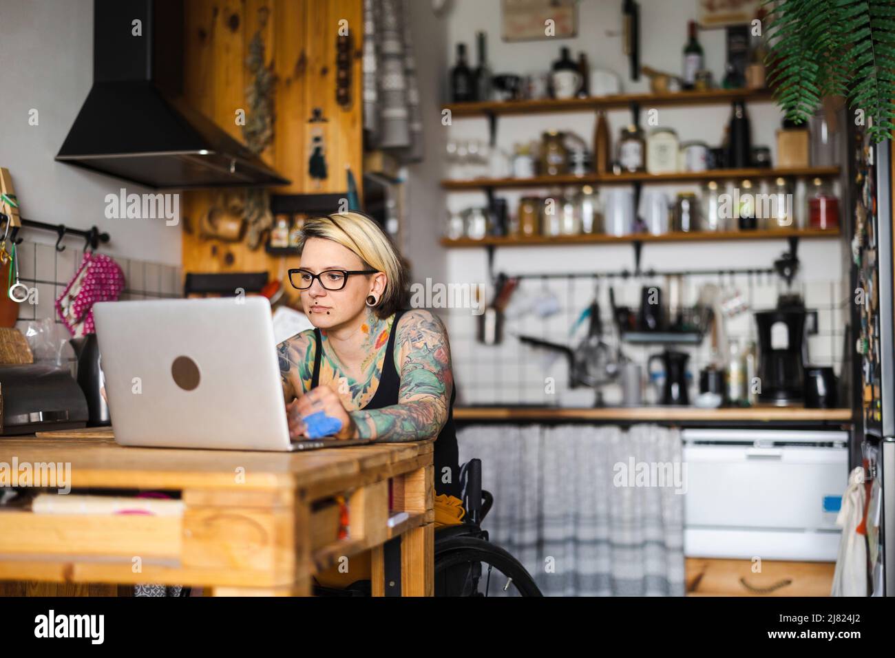 Junge tätowierte Frau im Rollstuhl, die zu Hause am Laptop arbeitet Stockfoto