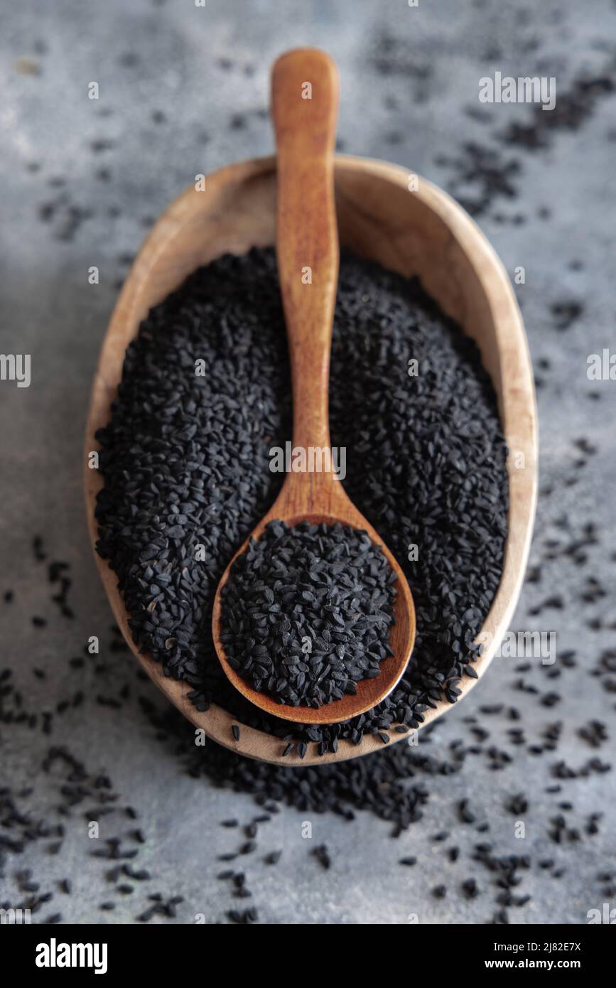 Indische Gewürze Schwarzkümmel (Nigella sativa oder Kalonji) Samen in Schüssel mit Löffel auf grauem Tisch Draufsicht. Traditionelle Medizin, gesunde und vegetarische foo Stockfoto