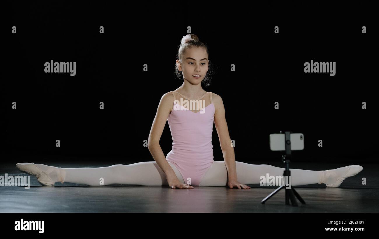 Mädchen Teenager Kind Ballerina akrobaten Turnerin sitzt auf dem Boden Tanzkurs Online-Unterricht mit Internet Trainer Trainer Lehrer aus der Ferne mit Smartphone auf Stockfoto