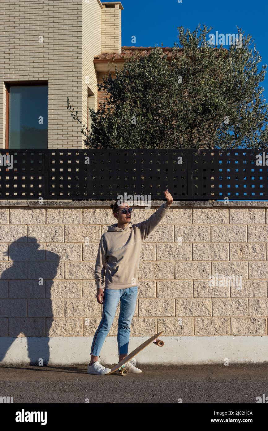 Vertikales Foto eines jungen Skaters, der sich mit der Hand vor der Sonne hütet und im Nachmittagslicht Schatten auf seinem Gesicht erzeugt Stockfoto