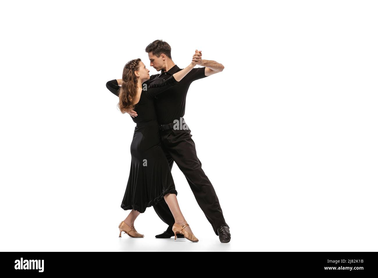 Zwei junge anmutige Tänzer tragen schwarze Bühnenoutfits und tanzen auf weißem Hintergrund isoliert den Tanzsaal. Konzept von Kunst, Schönheit, Musik, Stil. Stockfoto