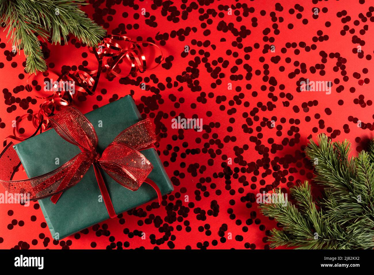 Eine grüne Geschenkbox mit einer roten Schleife auf einer roten mit Konfetti und einem Tannenzweig. Das Konzept von Weihnachten und Neujahr, Familienurlaub,. Stockfoto