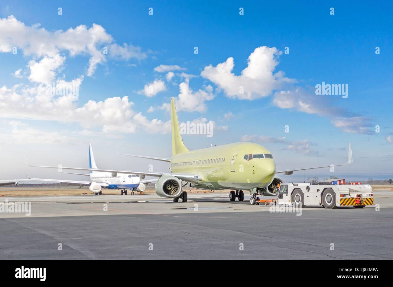 Abschleppwagen, der den Jet des Flugzeugs zum Parkplatz am Flughafen zurückschiebt. Eine weitere Ebene im Hintergrund Stockfoto