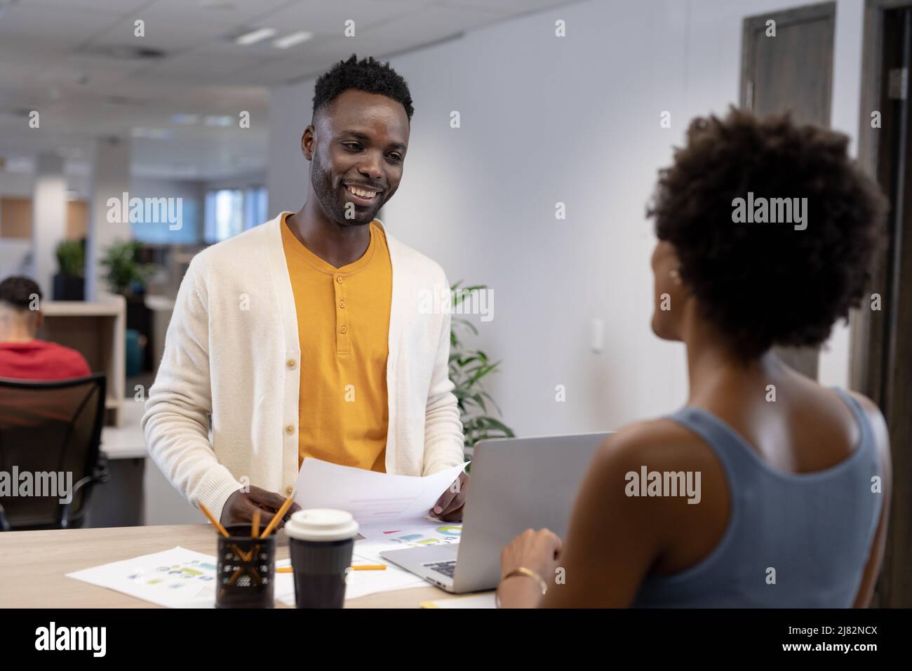 Lächelnder afroamerikanischer Geschäftsmann mit einer Geschäftsfrau mit Dokument- und Laptop-Aussehen am Arbeitsplatz Stockfoto