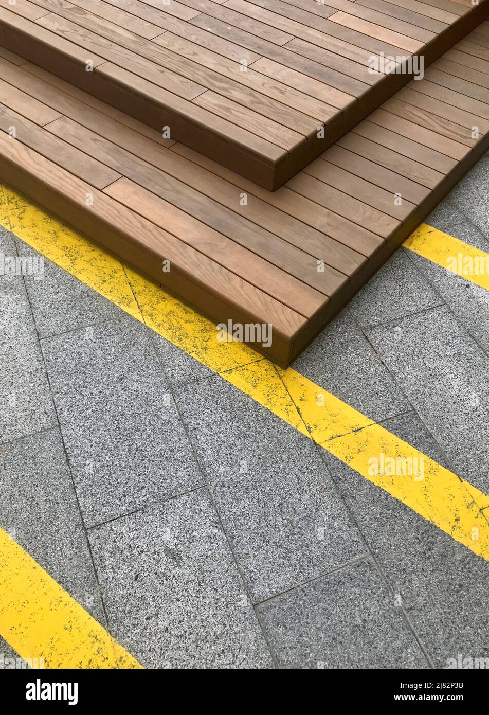Städtischer geometrischer moderner Hintergrund mit gelben Linien auf Betonfliesen und Holzkonstruktion. Stockfoto