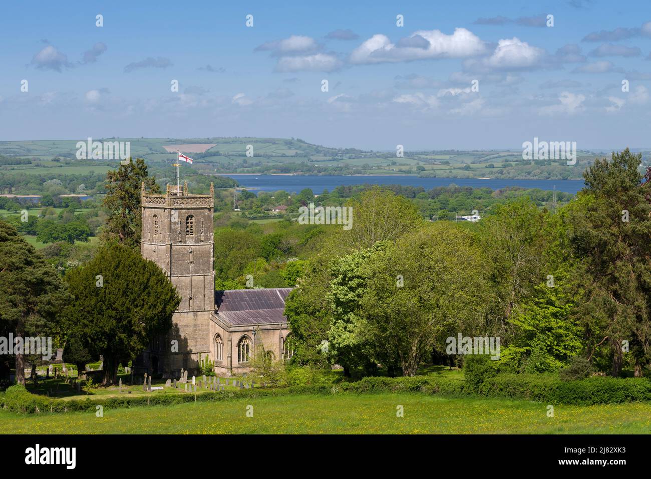 Die Kirche St. Michael des Erzengels im Dorf Compton Martin am Fuße der Mendip Hills mit dem Chew Valley Lake Reservoir im Jenseits, Somerset, England. Stockfoto