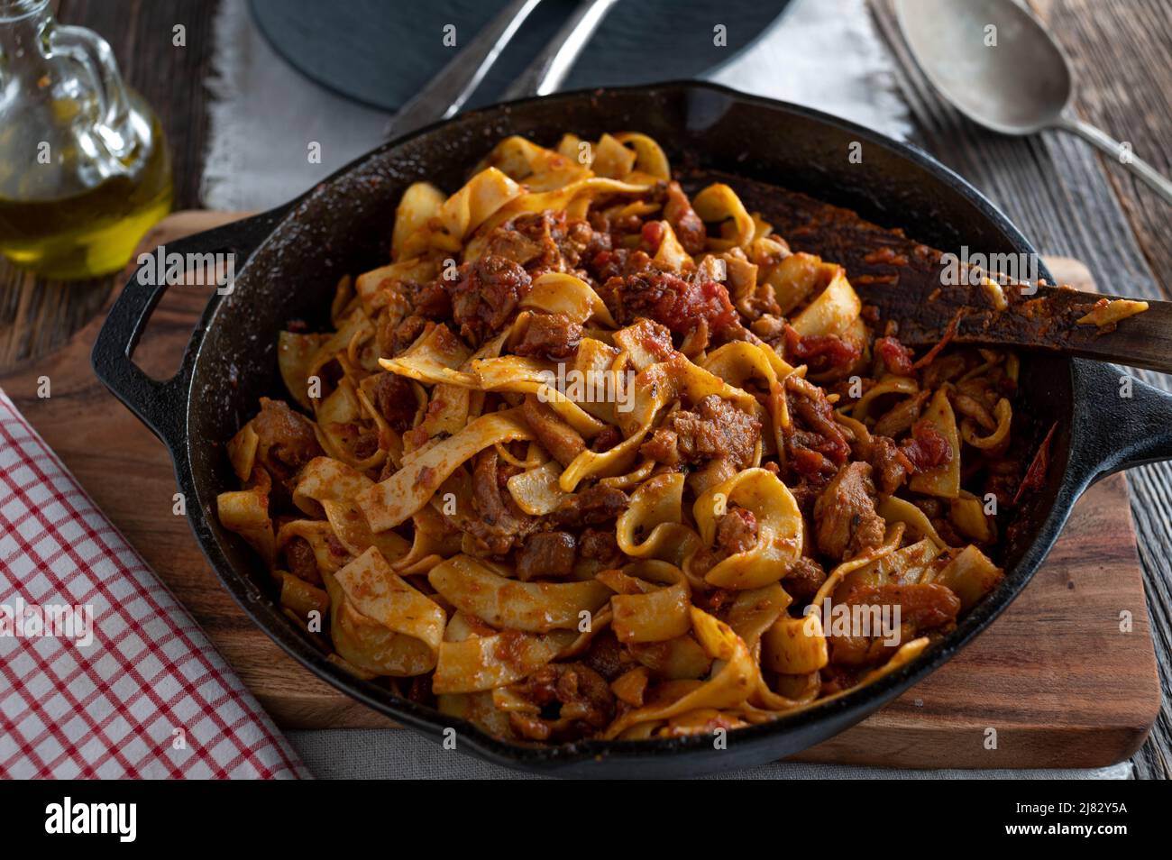 Geschmortes Hühnerfleisch mit Tomaten, Kräutersauce und Pasta in einer rustikalen gusseisernen Pfanne. Italienisches Gericht. Stockfoto