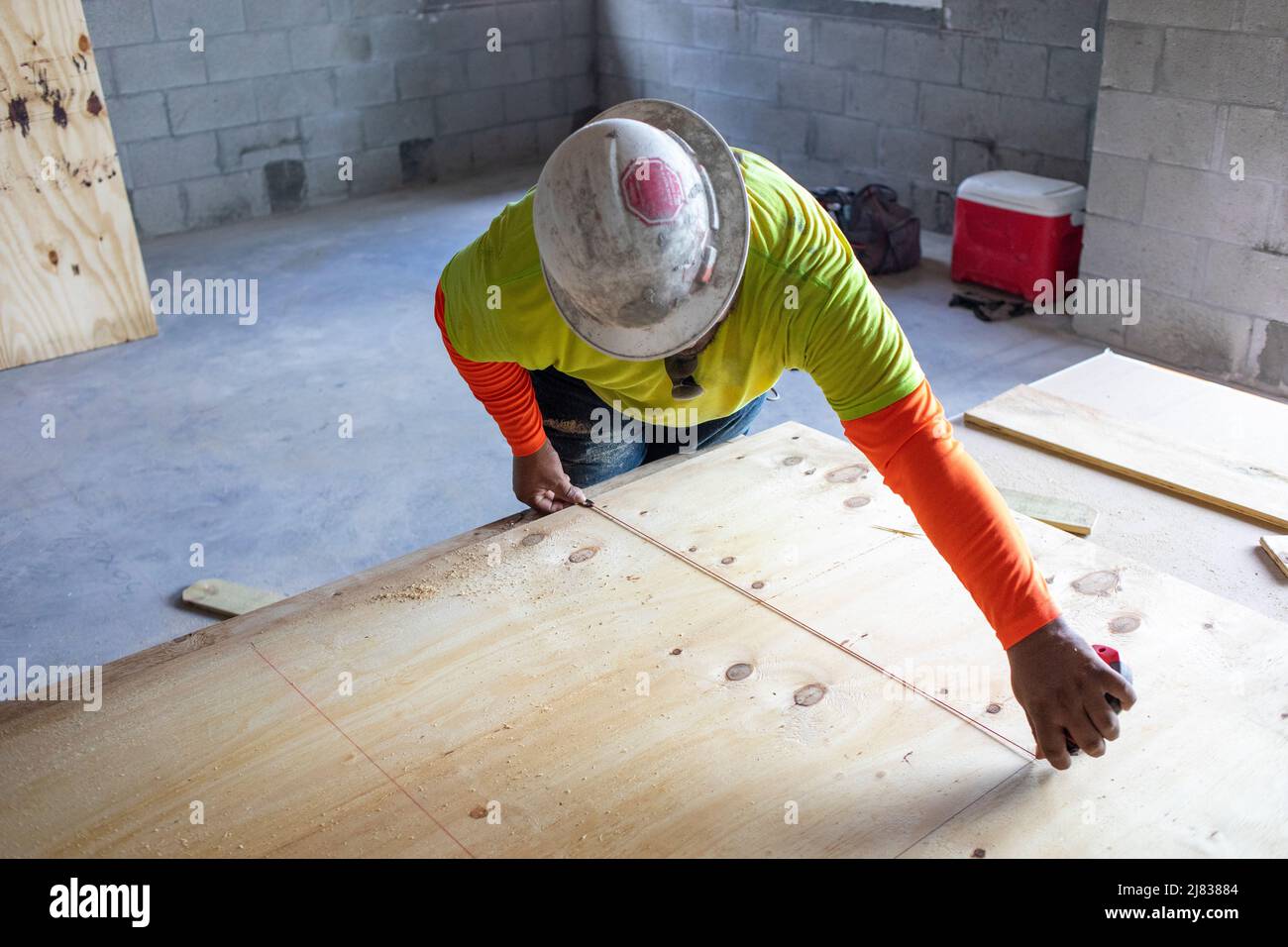 Ein Bauarbeiter misst ein Sperrholz, das im Wohngebäude wo nötig geschnitten und installiert werden soll. Stockfoto