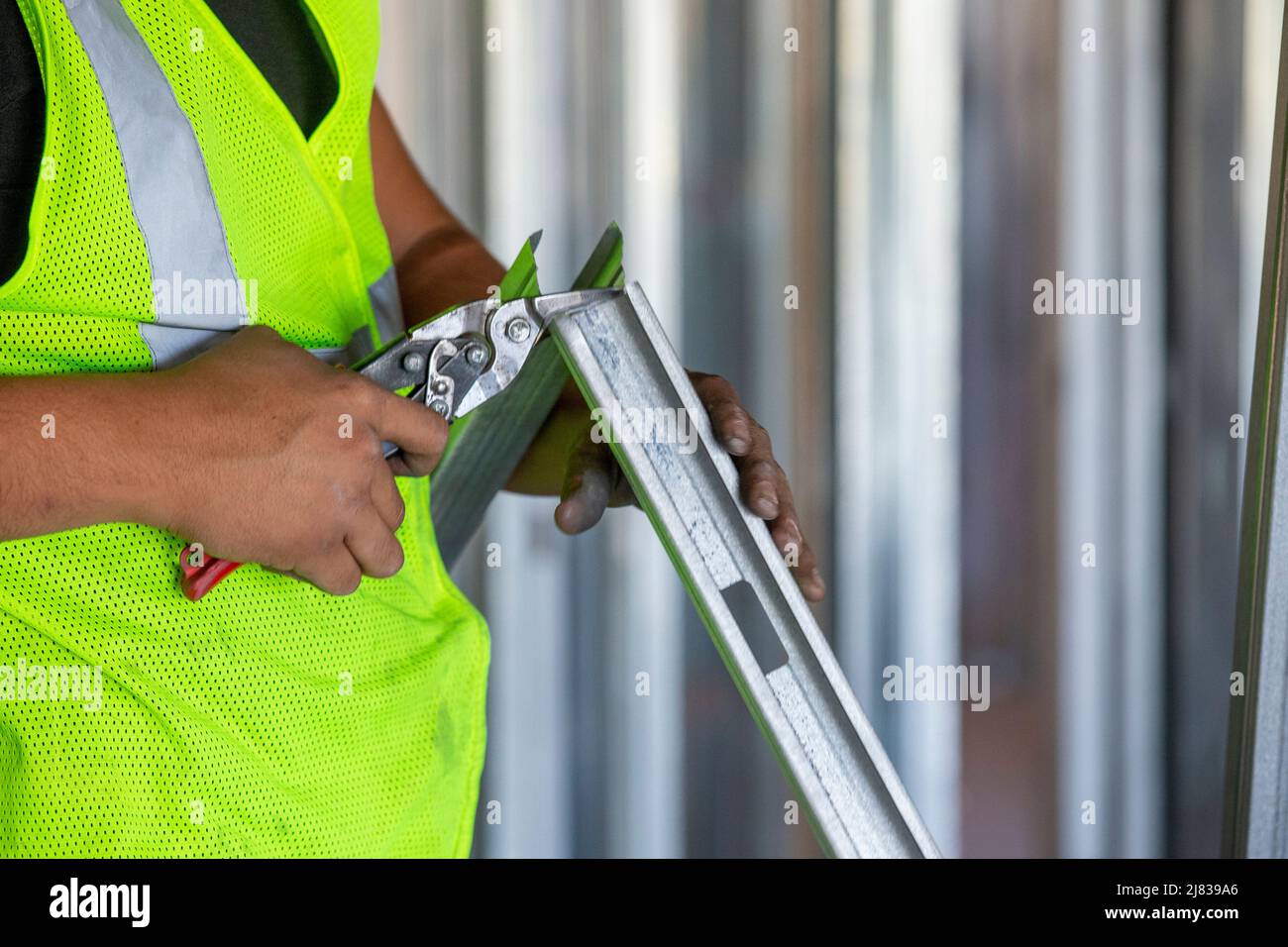 Ein Bauarbeiter/Rahmer schneidet einen verzinkten Stahlstab oder eine verzinkte Stahlstrebe mit einer Schneidzange für eine präzise Installation. Stockfoto