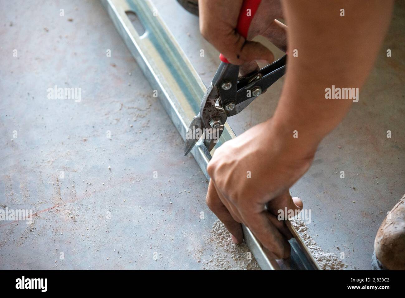 Ein Bauarbeiter/Rahmer schneidet einen verzinkten Stahlstab oder eine verzinkte Stahlstrebe mit einer Schneidzange für eine präzise Installation. Stockfoto