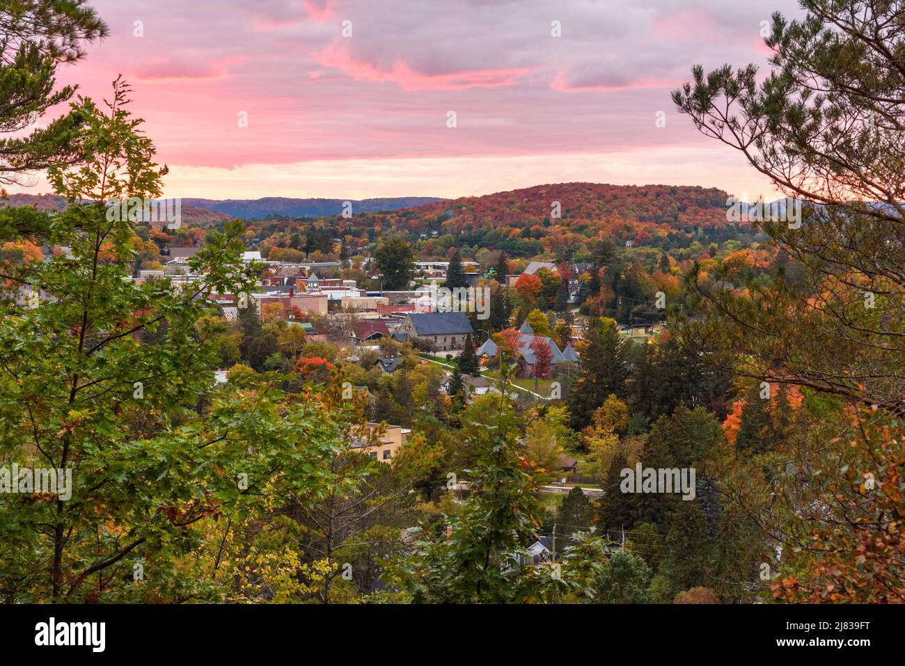 Blick von oben auf eine Stadt, umgeben von bewaldeten Hügeln auf dem Gipfel des Herbstlaubes in der Dämmerung. Huntsville, ON, Kanada. Stockfoto