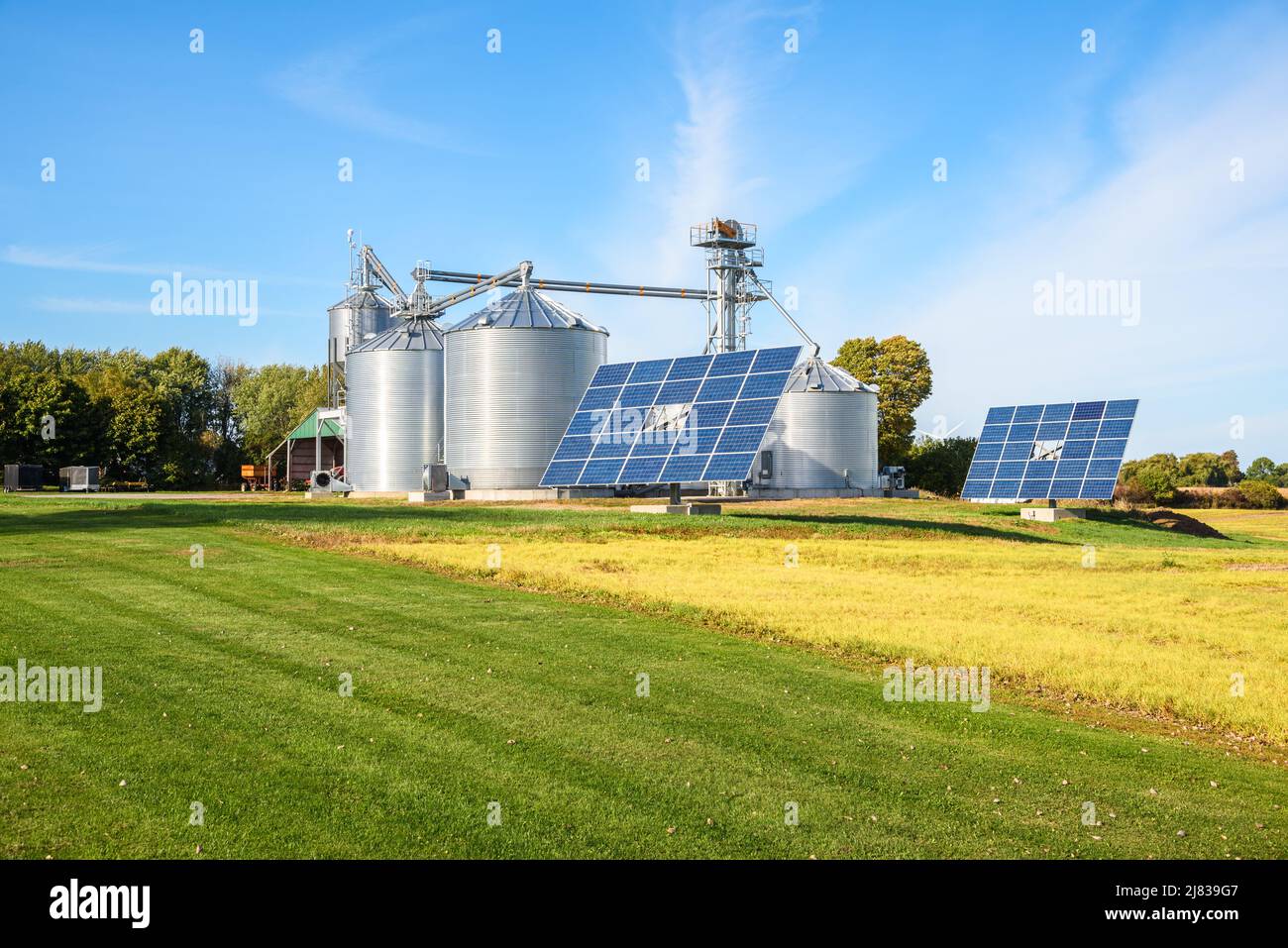 Sonnenkollektoren mit Getreideaufzug mit großen Stahllagerbehältern im Hintergrund in einem modernen Bauernhof an einem sonnigen Herbsttag Stockfoto