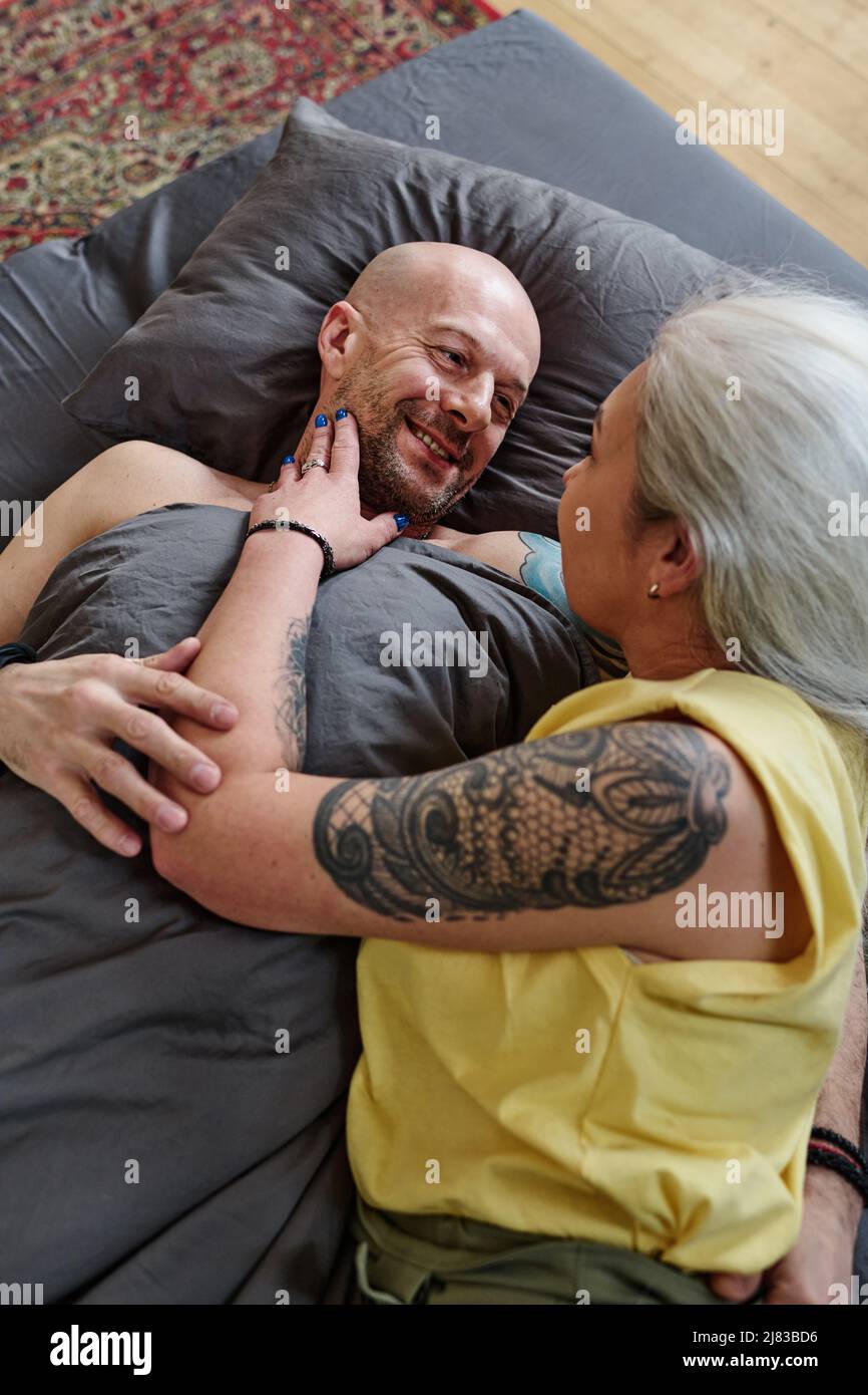 Reife Frau mit grauen Haaren und Tätowierungen am Arm, die sich im Bett entspannt und