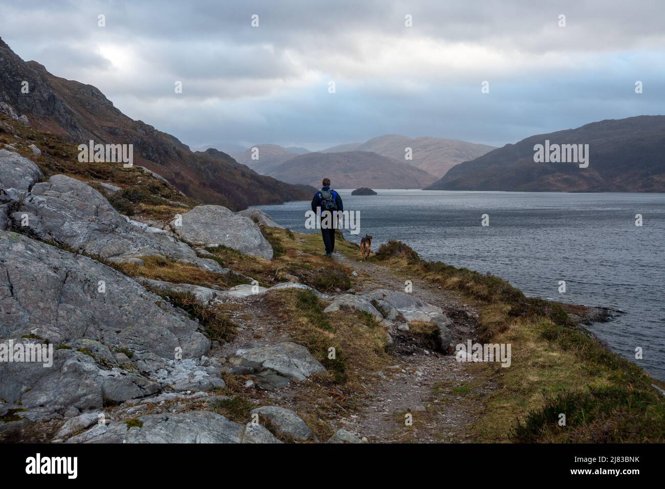 Landschaften in Großbritannien: Person, die im Winter einen Hund entlang des Loch Morar bei Mallaig läuft, schottische Highlands, Schottland, Großbritannien Stockfoto