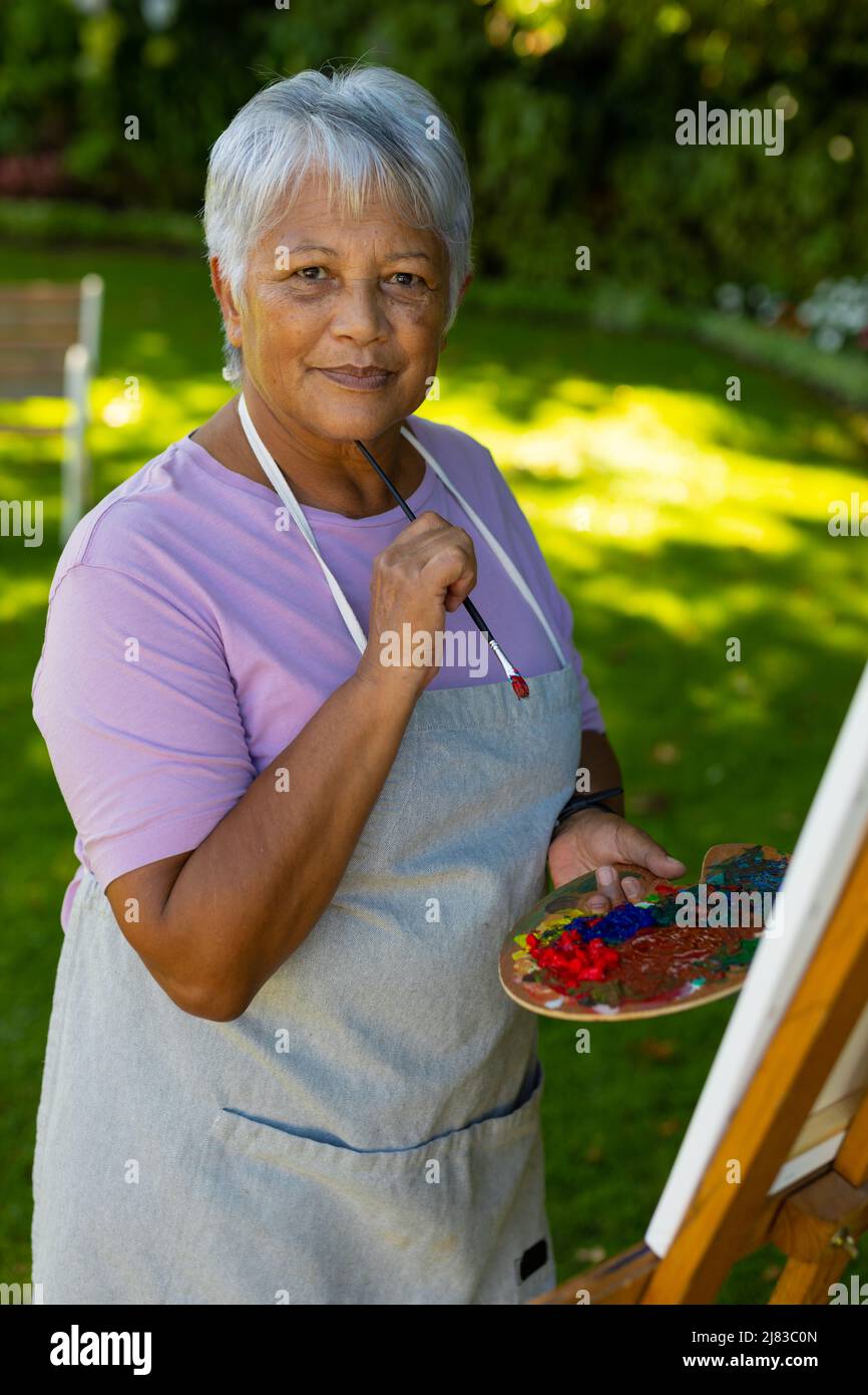 Porträt einer älteren Frau mit kurzen Haaren und Schürze, die Pinsel und Palette im Hof hält Stockfoto