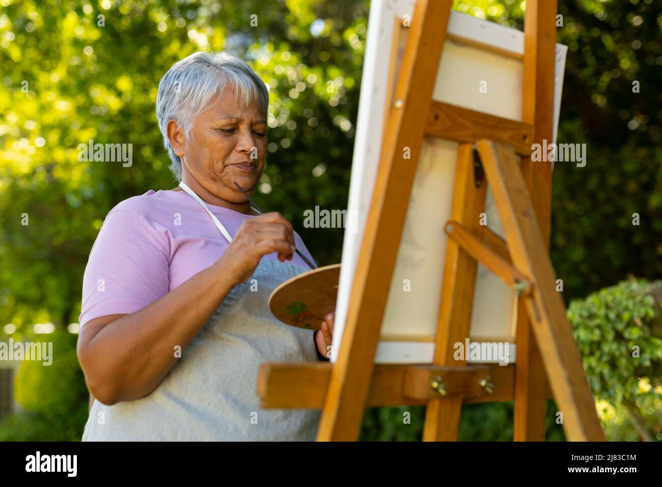 Low-Angle-Ansicht der Biracial Senior Frau mit kurzen Haaren Malerei mit Aquarellen auf Leinwand im Hof Stockfoto