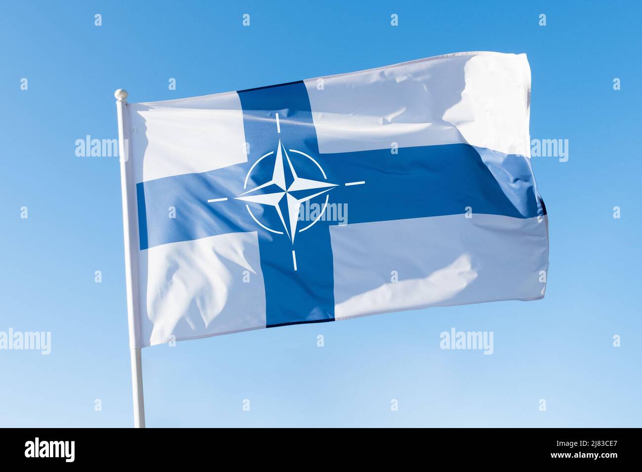 Finnland tritt dem NATO-Konzept bei. Finnische Flagge mit dem Emblem der NATO (North Atlantic Treaty Organisation) auf blauem Himmel. Stockfoto