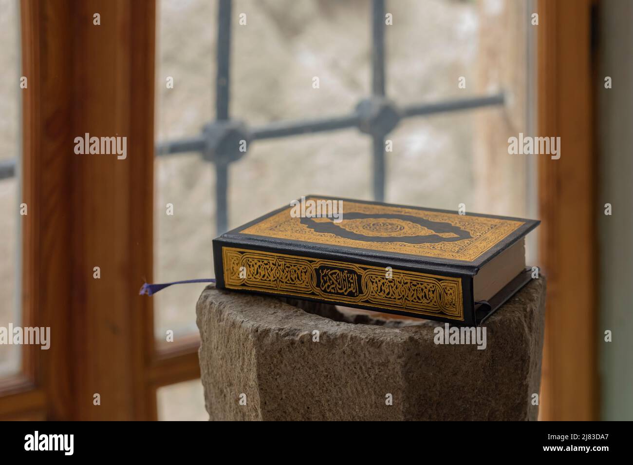 Nahaufnahme des Quran-Buches mit schwarz-goldener Einfassung auf einem Steinsockel neben einem hellen Fenster Stockfoto