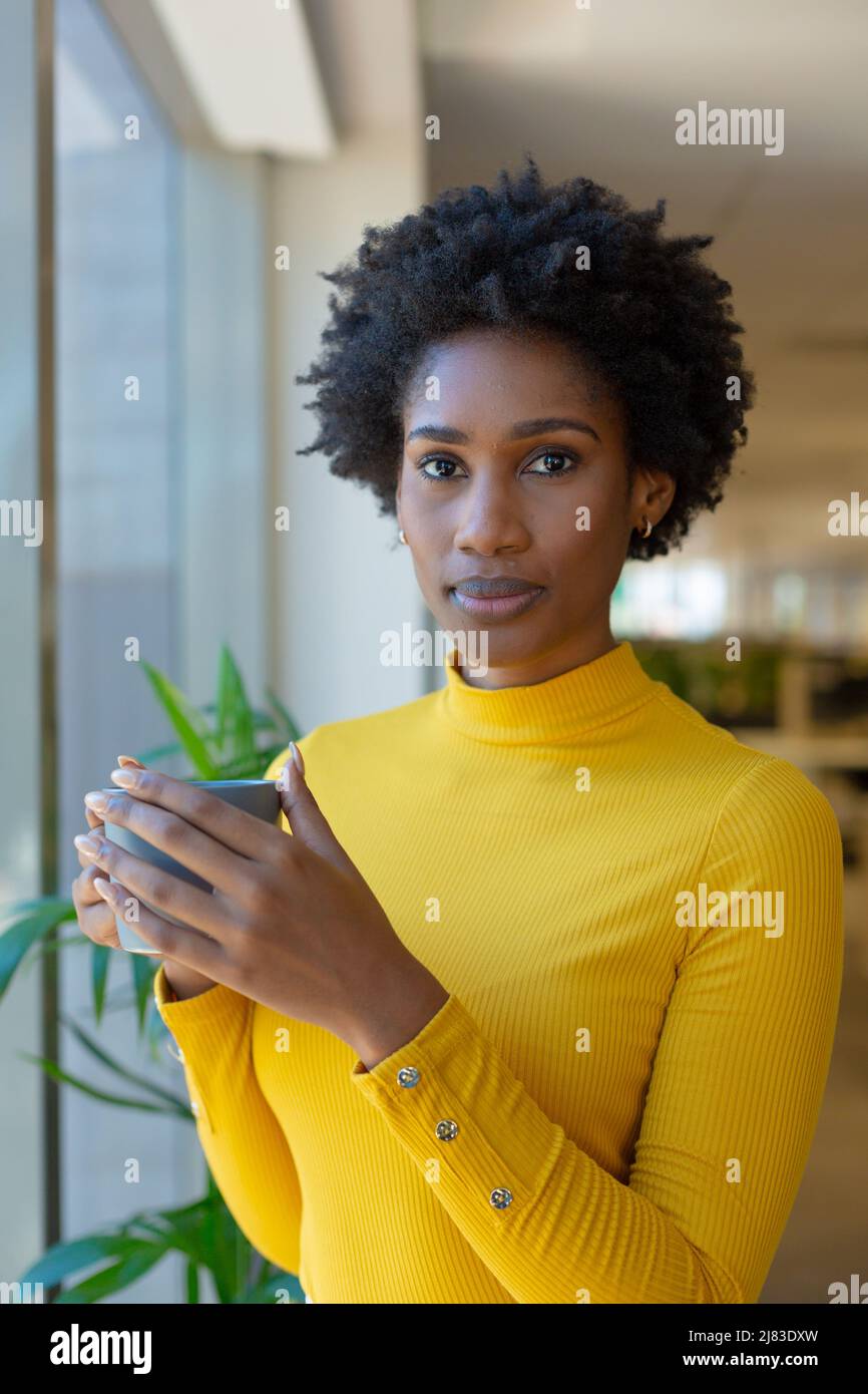 Porträt einer selbstbewussten afroamerikanischen Berater-Frau mit Afro-Frisur hält Becher am Arbeitsplatz Stockfoto