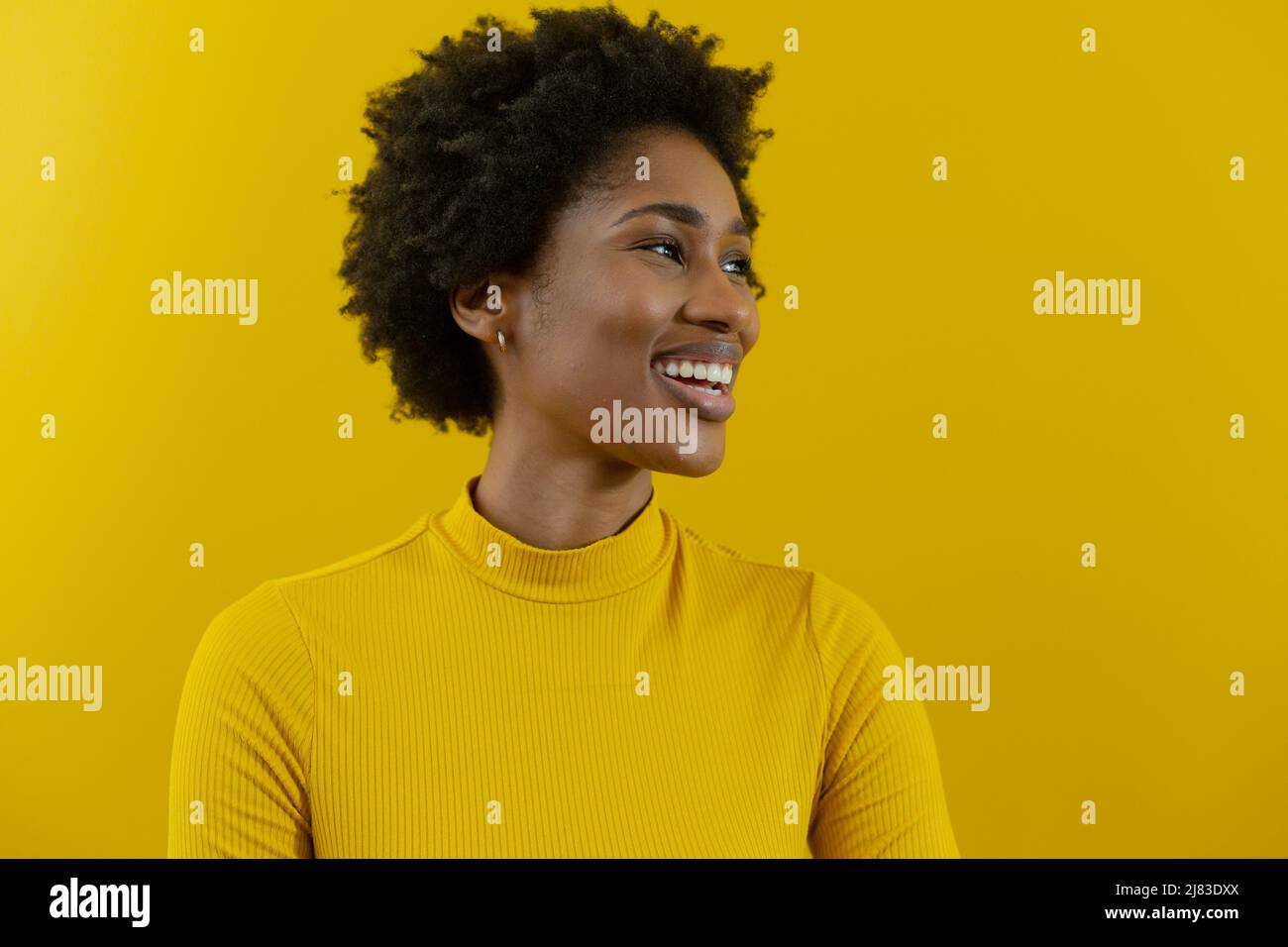 Fröhliche junge afroamerikanische Geschäftsfrau mit afro-Frisur, die gegen die gelbe Wand schaut Stockfoto